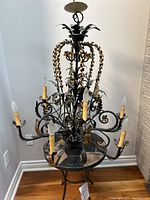 Full view of Tuscan style wrought iron chandelier with black and gold color scheme, showing candle-shaped bulbs and ornate leaf details.