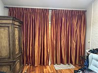 Two pleated silk drape panels hanging on a rod across a window