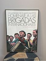 Full view of framed vintage poster showing group of men with accordion and Spanish text honoring International Brigades.