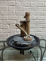 Front view of an indoor/outdoor decorative water feature with bamboo design and round black base on glass table against white brick wall