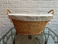 Side view of oval wicker basket with fabric liner and handles, displaying weave detail and neutral liner color.