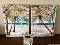 Two 18x24 inch beach scene oil paintings with palm trees and ocean, placed side by side with ceramic tissue cover in front.