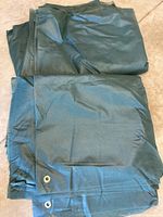 Two folded dark green frost blankets, one on top of the other, showing metal grommet in corner and material texture.