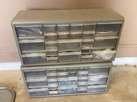 Photo showing two stacked metal storage cabinets with numerous clear plastic drawers filled with small metal hardware items like screws, nuts, and bolts.