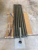 Photo showing six green metallic outer piping tubes, one metal base mount with square base plate, and two chrome tri-stabilization mounting hardware pieces all arranged on a concrete floor.