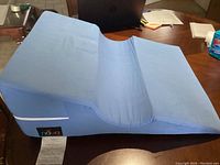 Blue Nova Ortho-Med bed wedge on a table with visible brand tag and fabric texture. Shows full side profile and top incline shape.