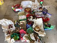 Overview of Christmas-themed items including ornaments wrapped in tissue paper, decorative tins, gift bags, and a serving dish arranged on the floor.