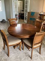 Front view of round wooden table with four wooden chairs with beige upholstered seats and wicker backs in a living room.