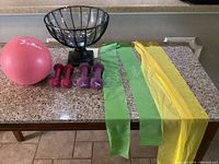 Photo showing pink Trideer ball, dumbbells, glass bowl on black metal stand, and stretch bands