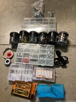 Photo showing all items in the hardware lot arranged on a concrete floor including organizers filled with screws, washers, tape rolls, bike repair kit, latch kit, and pouch.
