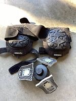 Photo showing a pair of Huskey black knee pads for tile and floor workers with adjustable Velcro straps and a deformable LED garage ceiling light with four adjustable white panels for directional lighting.