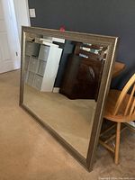 Image of the large rectangular mirror leaning against a wall, showing the reflective surface and silver-textured frame.