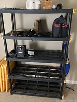 Front view of the large black plastic 5 tier shelving unit with various small items on top shelves, showing unit's condition and structure