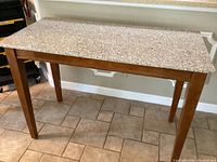 Full view of the high top marble dinette table showing wooden legs and speckled marble top surface.