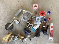 Photo showing assorted plumbing parts including hose connectors, clamps, valves, Teflon tape, and sealant.