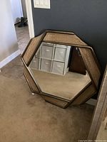 Hexagonal wall mirror leaning against gray wall, showing the six-sided shape and textured frame.