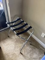 Luggage stand positioned indoors against a beige wall, showing full frame and fabric straps.