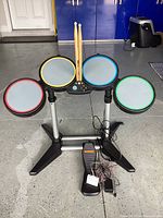 Front view of an Xbox electronic drum set with four colored drum pads, foot pedal, and wooden sticks.