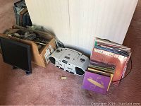 Overview of the lot showing the vinyl record stack, white boombox, computer monitor, and box of cables on carpet