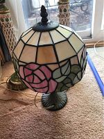 Tiffany style stained glass lamp shade with cream, pink, and green floral design and ornate black metal base with finial