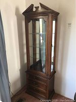 Full view of wooden curio cabinet showing wood finish, glass door with shelves inside, and three drawers below.