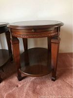 Front view of one oval wooden end table showing carved detail, slide-out shelf, and bottom shelf