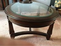 Front-left angle of the oval glass top coffee table showing carved wood frame and legs.