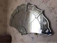 Fan-shaped mirror mounted on floral wallpapered wall showing intricate floral and leaf pattern etching on segments.