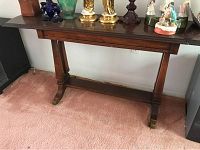 Full view of wooden sofa table showing drop leaf ends, decorative legs, and stretcher base with brass foot caps, placed on pink carpet.
