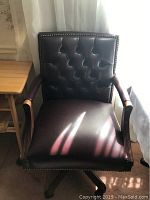 Front view of executive tufted leather chair with brass rivets and wooden arms.