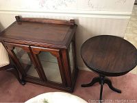 Glass display cabinet with two glass doors and two shelves next to round parlor table