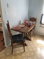 Drop leaf dinette table with two wooden chairs and blue floral cushions, with pink glass dinnerware on table