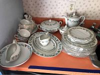 Full view of all vintage Japanese fine china items arranged on a countertop, including teapot, serving bowls, plates, cups, and saucers in a blue-green leaf pattern with gold trim.