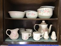 Photo of china set displaying teapot, creamer, teacups, lidded bowls, and salt and pepper shakers on two shelves