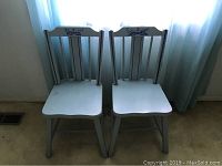 Front view of two vintage light blue wooden children's chairs showing decorative painted top backrest and contoured wooden seats