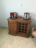 Full view of wooden wine cabinet with door and bottle storage section, plus items on top including rotating glass holder and boxed items.