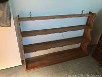 Full view of the wooden four shelf wall unit showing all shelves and side supports, placed on carpeted floor.