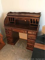 Roll top desk with upper decorative trim, vertical compartments, and multiple drawers on both sides, showing overall front view.