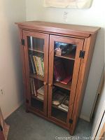 Front view of wooden two door book cabinet with glass doors showing contents inside.