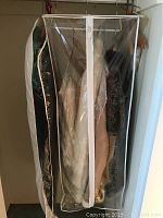 Photo of multiple jackets and sweaters hanging on a rack inside a clear plastic garment bag.