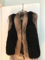 Front view of a women's fur vest hanging on a hanger showing black fur panels on the sides with light brown fur down the center front and collar area.