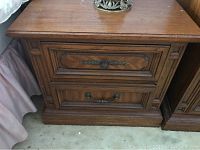 Front view of one wooden end table showing two drawers with decorative metal handles and carved wood panels.