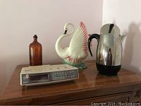Full lot showing amber glass bottle, swan lamp, Sylvania clock radio, and percolator on wooden surface