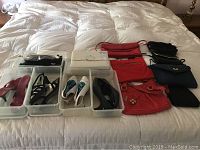 Overview of shoes in plastic trays and assorted purses laid out on bed.