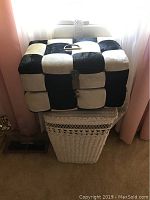 Full view of the checkered storage box sitting on top of the white wicker hamper.