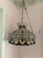 Single vintage hanging lamp with decorative scalloped edge glass panels and brass metal frame hanging from chain on ceiling.