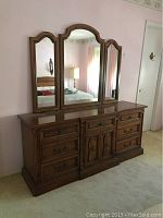 Front view of full size dresser with attached triple mirror showing multiple drawers and central cabinet with decorative panels and handles.