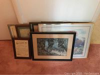 Seven framed wall art pictures stacked against a wall on floor showing various sizes and frame styles