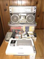 Vintage short wave radio boombox on top of plastic bin, with Lexmark printer and assorted tapes below
