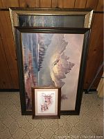 Five framed wall art pieces leaning against wood-paneled wall, shows front views revealing mountain landscape, deer print, floral art